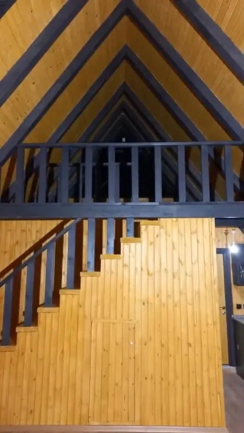 Ahşap kaplamalı A tipi bungalovda siyah korkuluklu galeri katı ve merdiven