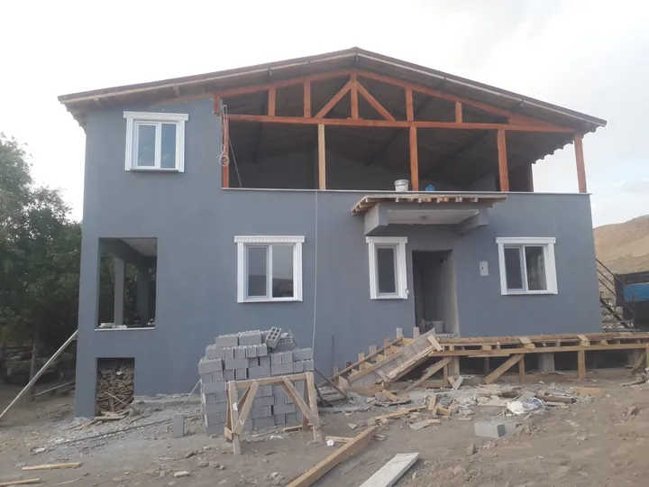 Gri dış cepheli iki katlı yapıda ahşap çatı konstrüksiyonu ve şantiye alanı
